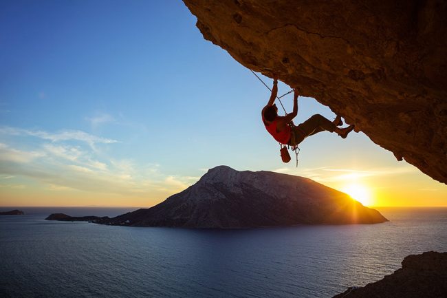 young-man-climbing-overhanging-cliff-at-sunset-PVT5LRV