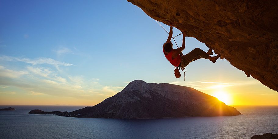 young-man-climbing-overhanging-cliff-at-sunset-PVT5LRV